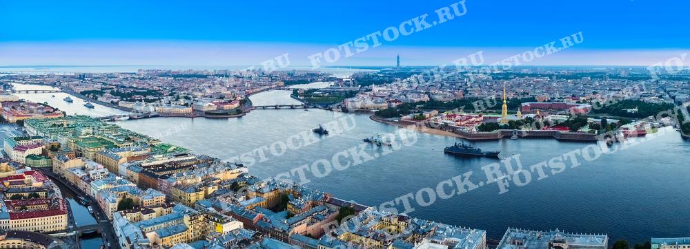 На этой фотопанораме представлен вечерний или утренний вид на Санкт-Петербург с воздуха. Городской пейзаж охватывает изгибы реки Невы, многочисленные мосты, архитектурные ансамбли и протяженные набережные. Военные корабли в акватории Невы иллюстрируют темы российского флота и подготовки к параду.